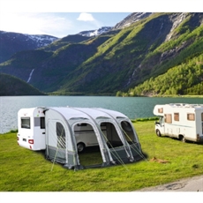Förtält med bågar och fönster vid husvagn nära sjö och berg.